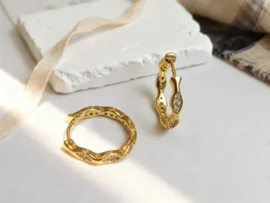 Detaillierte Nahaufnahme von goldenen Wellen-Ohrringen mit funkelnden Kristallsteinen