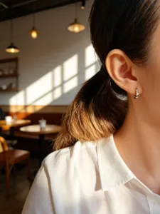 Nahaufnahme eines minimalistischen S925 Sterlingsilber-Ohrrings am Model im Café
