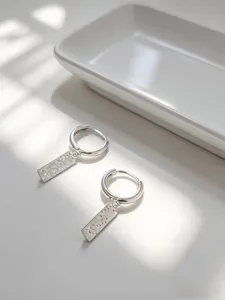 Dettaglio di orecchini a cerchio in argento con pendente rettangolare texturizzato