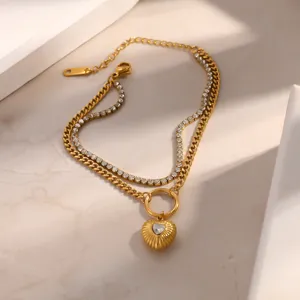 Dettaglio di bracciale a doppio strato in acciaio dorato con ciondolo a cuore di cristallo.