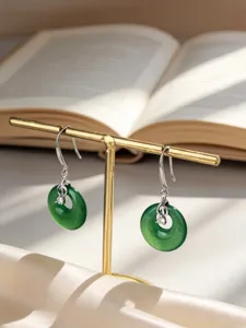 Elegantes pendientes de dona verde con notas musicales en un soporte de joyería dorado.