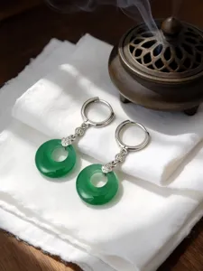 Primo piano elegante di orecchini a ciambella in giada verde su seta bianca con incenso