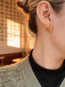 Eleganter gewellter goldener Creolen-Ohrring mit Steinen in der Nahaufnahme am Modellohr