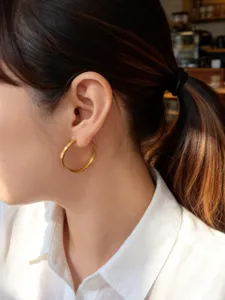 Primer plano de un elegante pendiente de aro dorado con textura de escamas en una modelo