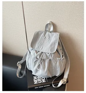 Detailansicht eines hellgrauen Nylon-Rucksacks mit Kordelzug und Stickerei auf einem Buch.