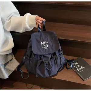 Detailansicht eines dunkelblauen Nylon-Rucksacks mit Kordelzug und MUT ING-Stickerei auf Holzstufen