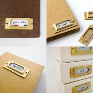 Detailaufnahme von Vintage Messing Etikettenhaltern auf Notizbüchern und Aufbewahrungsboxen.