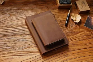 Detailaufnahme von braunen Leder-Notizbuchhüllen und Notizbüchern auf einem rustikalen Holztisch.
