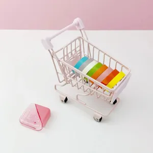 Detailed shot of a cute mini metal shopping cart filled with colorful tape rolls on a white table.