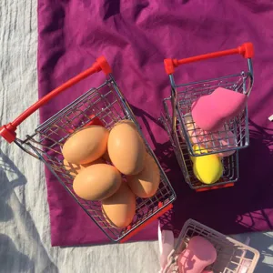 Mini metal shopping cart desktop organizer with makeup sponges and props for photography and home decor.