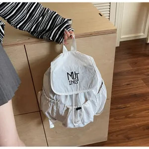 Weißer Nylon-Rucksack mit Kordelzug und MUTING-Stickerei vor einem Holzinterieur