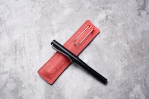 Gros plan d'un étui à stylo en cuir rouge gaufré avec un stylo plume noir sur fond texturé.