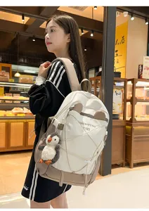 Lifestyle-Ansicht eines cremeweißen Studenten-Rucksacks mit Pinguin-Anhänger