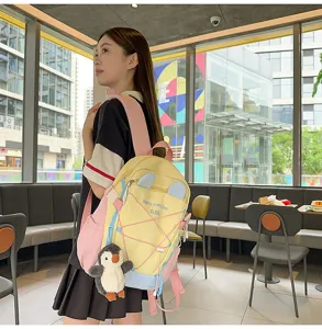 Seitenansicht eines gelb-rosa Schüler-Rucksacks mit Pinguin-Anhänger am Modell