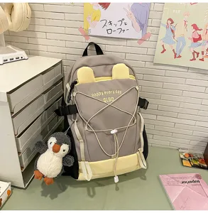 Detailansicht eines großen grauen und gelben Schulrucksacks mit Plüschpinguin-Anhänger.