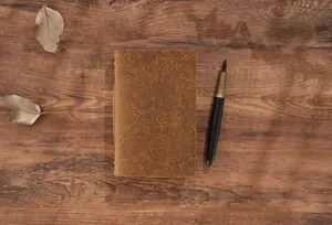 Detailansicht des retro gepraegten Leder Notizbuchs auf rustikalem Holztisch mit Fuelle.
