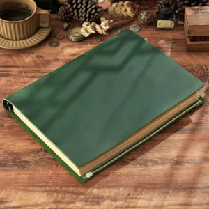 Dettaglio di un taccuino con risvolto in pelle verde vintage su un tavolo in legno.