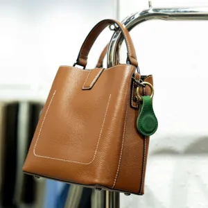 Brown genuine leather top handle handbag with green magnetic clip accessory detail view.