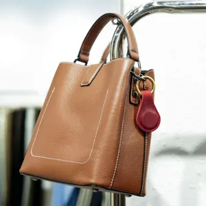 Detail view of brown leather handbag featuring fine stitching, metal hardware and red pendant.