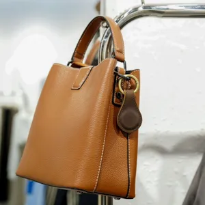 Close-up of brown genuine leather bucket bag with metal hardware and stylish charm detail.