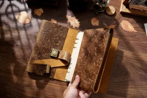Primer plano de cuaderno de cuero grabado vintage en mesa de madera con hojas de otoño.