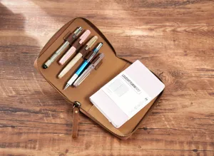 A6 leather zipper planner cover with pen holders and notebook insert on wooden background.