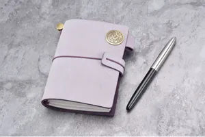 Dettaglio del taccuino da viaggio in pelle viola con chiusura in metallo vintage e penna.