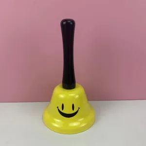Campana de mano de metal amarillo con mango negro y cara sonriente para juegos escolares.