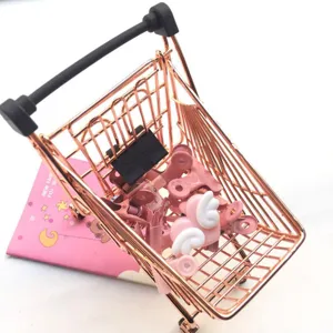 Detail view of miniature rose gold shopping cart, cute desktop storage organizer props.