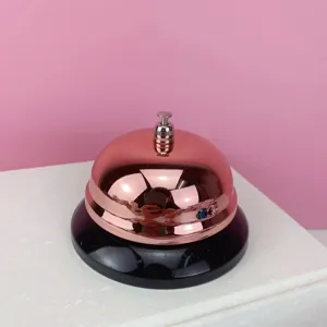 Detalle de cerca de un timbre de servicio en oro rosa y negro, ideal para mostrador.