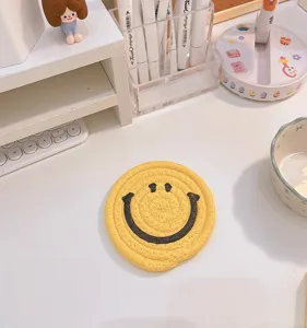 Cute yellow braided cotton rope coaster with black smiley face design for table decor.