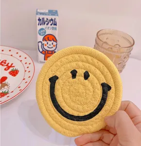 Cute ins-style yellow woven cotton rope coaster with black smiley face pattern for table decor.