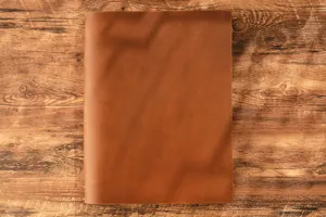 Dettaglio di un quaderno diario in pelle marrone vintage crazy horse su tavolo in legno.