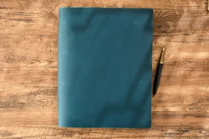 Dettaglio taccuino A4 vintage con anelli in vera pelle, copertina blu con penna stilografica.