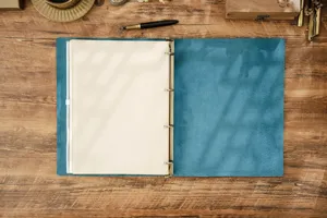 Vista dettagliata ravvicinata di un quaderno con anelli in vera pelle blu su tavolo di legno.