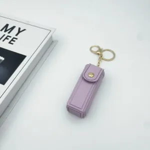 Close up detail view of a stylish purple leather lipstick case keychain with gold tone hardware.