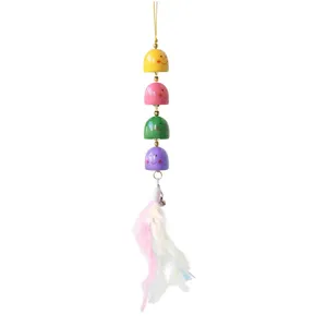 Close-up of colorful wooden smiley bell pendant with soft feather tassel, hanging detail shot.