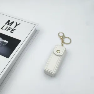 White leather lipstick case keychain detail view, portable makeup holder with gold hardware.