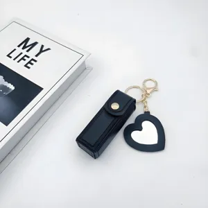 Close-up detail of the black leather lipstick case keychain with a cute heart mirror pendant.