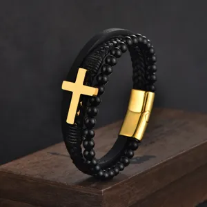 Close-up showing the texture of the black braided leather and polished gold cross bracelet.