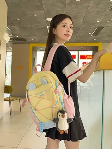 Süßer gelb-blauer Schulrucksack mit Pinguin-Plüschanhänger, getragen von Model im Café.