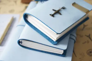 Quaderno da viaggio in pelle azzurra con dettaglio charm in metallo aereo sul tavolo