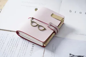 Quaderno di viaggio in pelle rosa con clip metallica e ciondolo occhiali per diario.