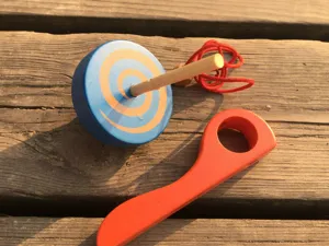 Vista de detalle de peonza de madera con cuerpo azul y mango rojo sobre superficie.