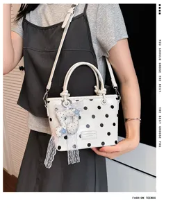 Elegante weiße Handtasche mit schwarzen Punkten und dekorativem Musiknoten-Anhänger.