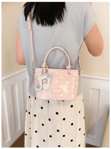 Detail einer rosa gepunkteten Beuteltasche mit Musiknoten-Anhänger, getragen von einer Person.