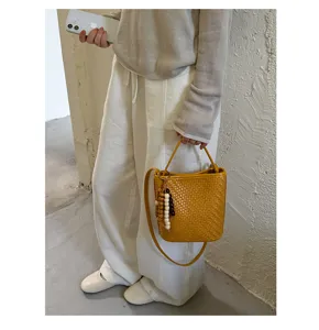 Close-up of a mustard yellow woven bucket bag with a wooden bead tassel charm