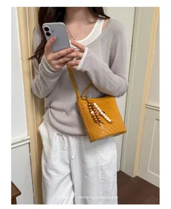 Mustard yellow woven leather bucket bag with bead charm shown in lifestyle commute setting
