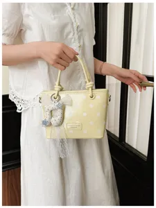 Gelbe gepunktete Beuteltasche am Arm eines Models vor einer weißen Spitzenbluse