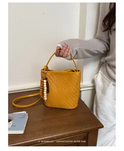 Sophisticated yellow woven bucket bag with retro wooden beads charm on a vintage desk
